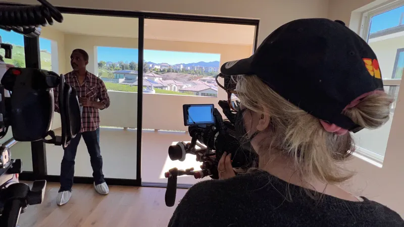 An over-the-shoulder view of a camera operator filming a subject indoors