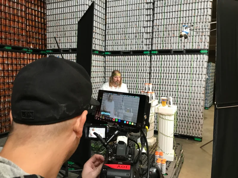 Camera operator filming an interview against a wall of cans