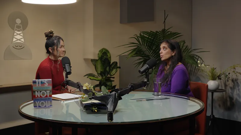 Two speakers seated at microphones on a warmly lit interview set