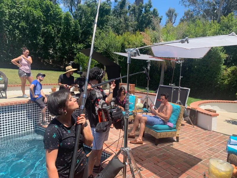 A camera crew, boom microphone, and lighting equipment beside a pool