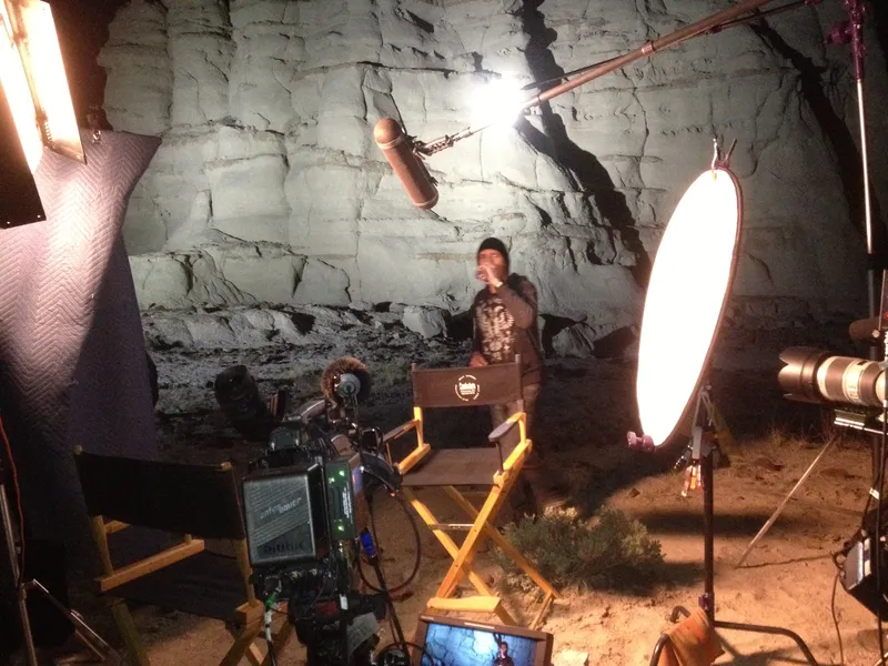A camera, boom microphone, and lights arranged around a rock-wall set